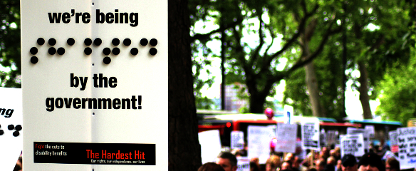 Photo of a banner from the Hardest Hit March in 2011 featuring the message "we're being shafted by the government" - with the word shafted written in braille.